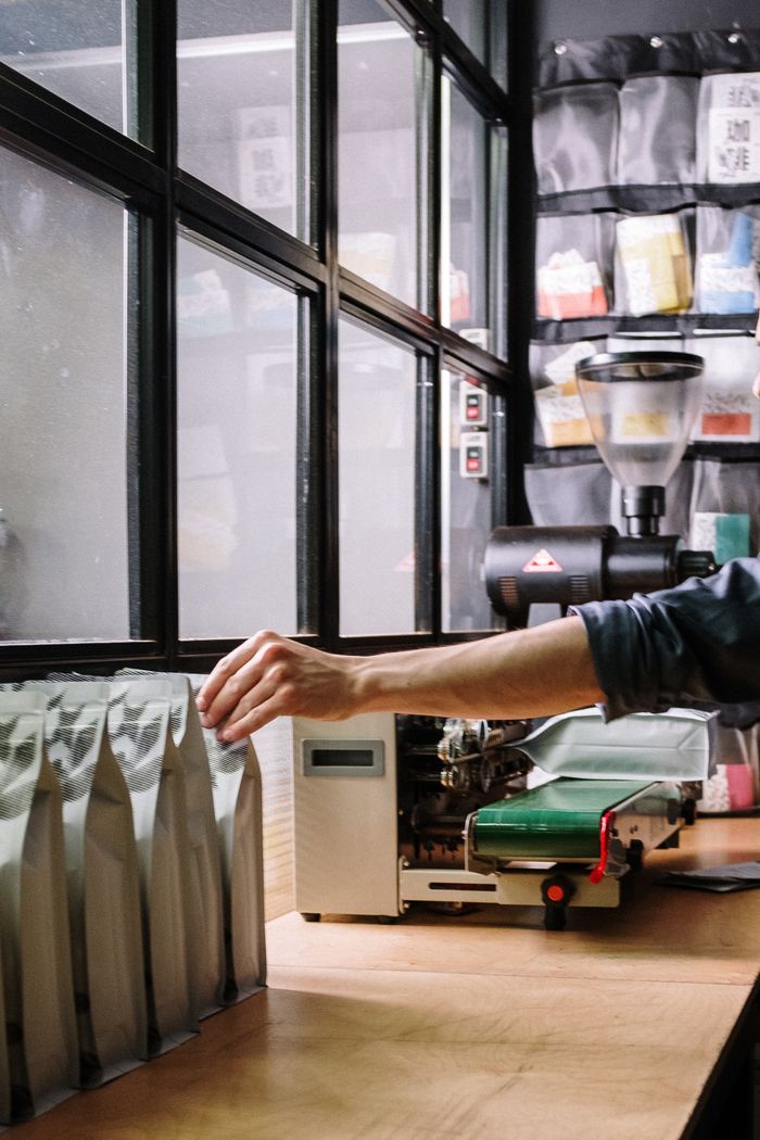 A worker packs coffee bags in an industrial workshop setting with machinery.